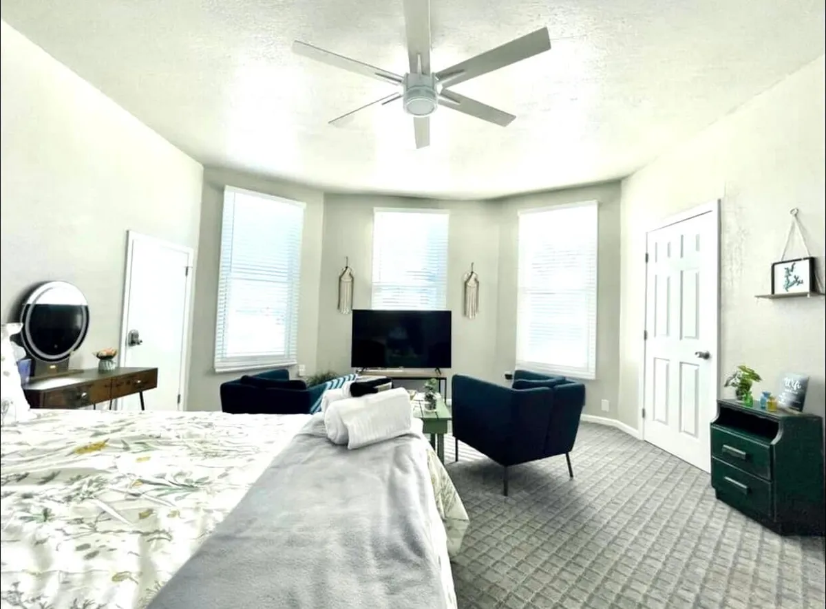 A cozy and comfortable sleeping area with a bed dressed in floral bedding. Two armchairs and a television provide additional options for relaxation or conversation. A side table with a mirror adds a residential touch, and the room's warm lighting enhances its inviting mood.