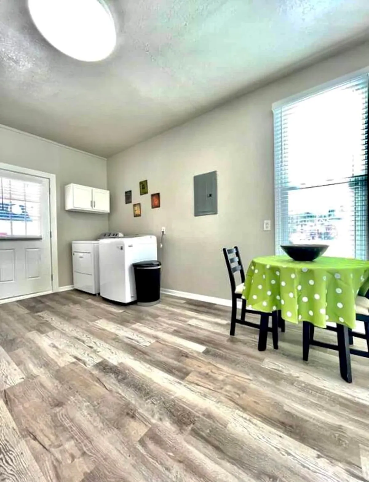 A bright and functional dining space with a green polka dot tablecloth, white appliances, and a black chair. The space is airy and conducive to casual dining, socializing, or completing home tasks such as laundry.
