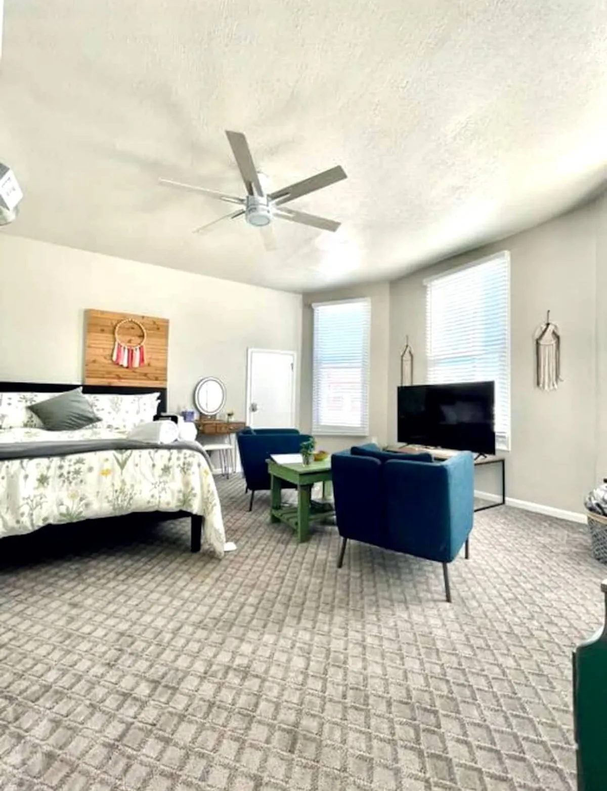 Featuring the floral-bedded room with blue chairs, a green table, and a television, this image showcases an inviting spot to relax, watch TV, or converse after enjoying the neighborhood’s dining scene. The overall atmosphere is serene and perfect for evening unwinding.