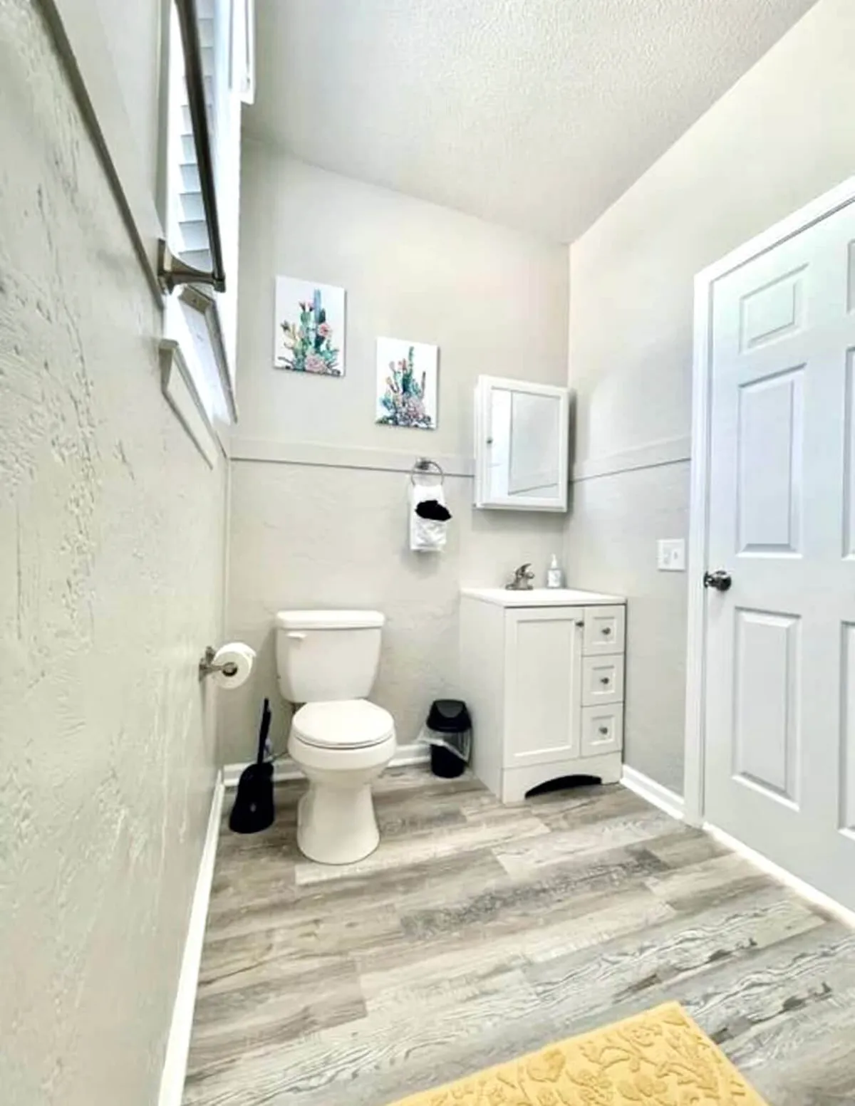 A serene bathroom space featuring a clean vanity with a mirror, a well-placed toilet, and tasteful wall artwork. The neutral palette and uncluttered surfaces contribute to a calm, spa-like environment ideal for relaxation and daily routines.